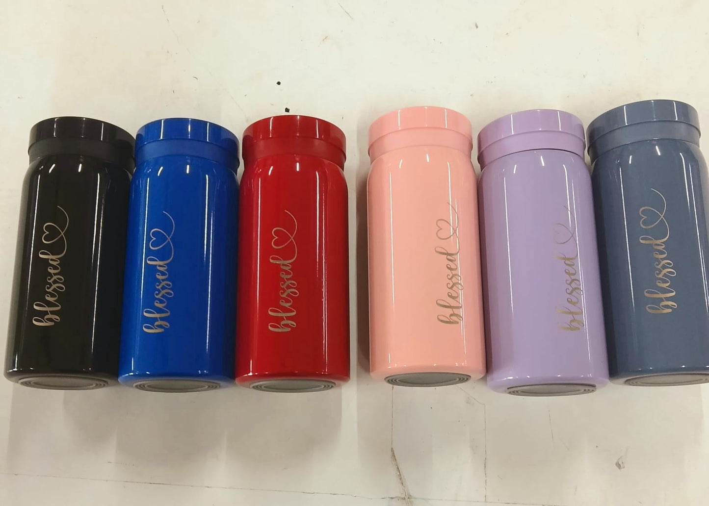 Six cylindrical containers in black, blue, red, pink, purple, and gray with 'blessed' text on a white background.